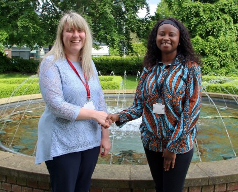 Two women shaking hands standing in front of a water fountain.